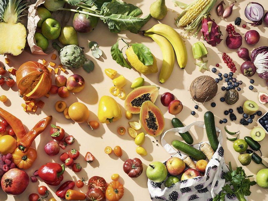 Vielfseitiges frisches Obst und Gemüse liegt auf einem beigefarbenen Untergrund