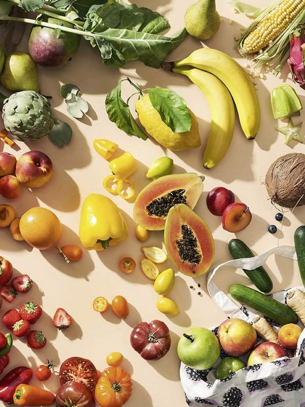 Vielfseitiges frisches Obst und Gemüse liegt auf einem beigefarbenen Untergrund