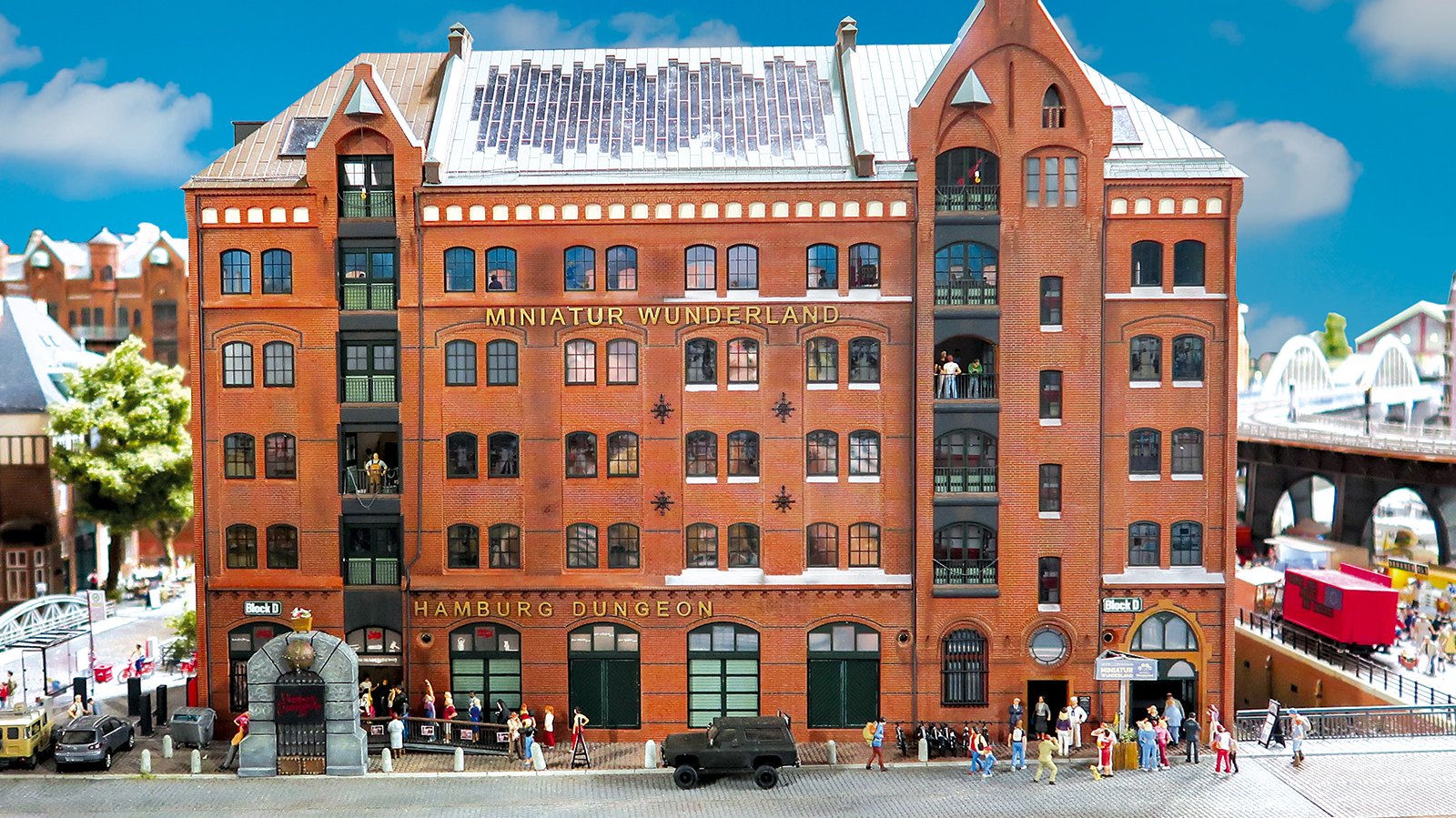 Nachbildung Miniatur Wunderland. Großes, rotes Backsteinhaus in der HH Speicherstadt mit goldenem Schriftzug Miniatur Wunderland, blauer Himmel, Schäfchenwolken