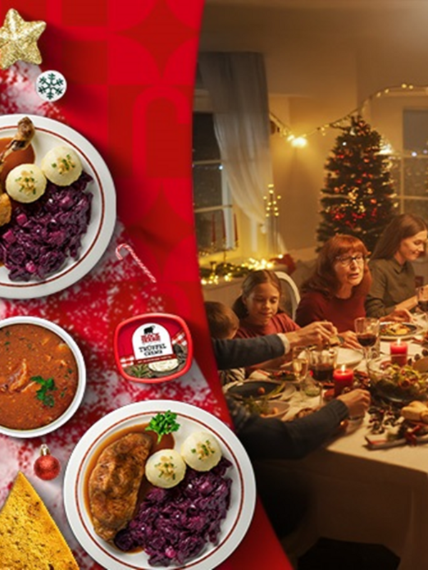 Tisch voller klassichen Köstlichkeitengedeckt mit roter Tischdecke und BlockHouse Creme. Daneben sitzt eine Familie am gedeckten Tisch im Hintergrund ist ein geschmückter Weihnachtsbaum