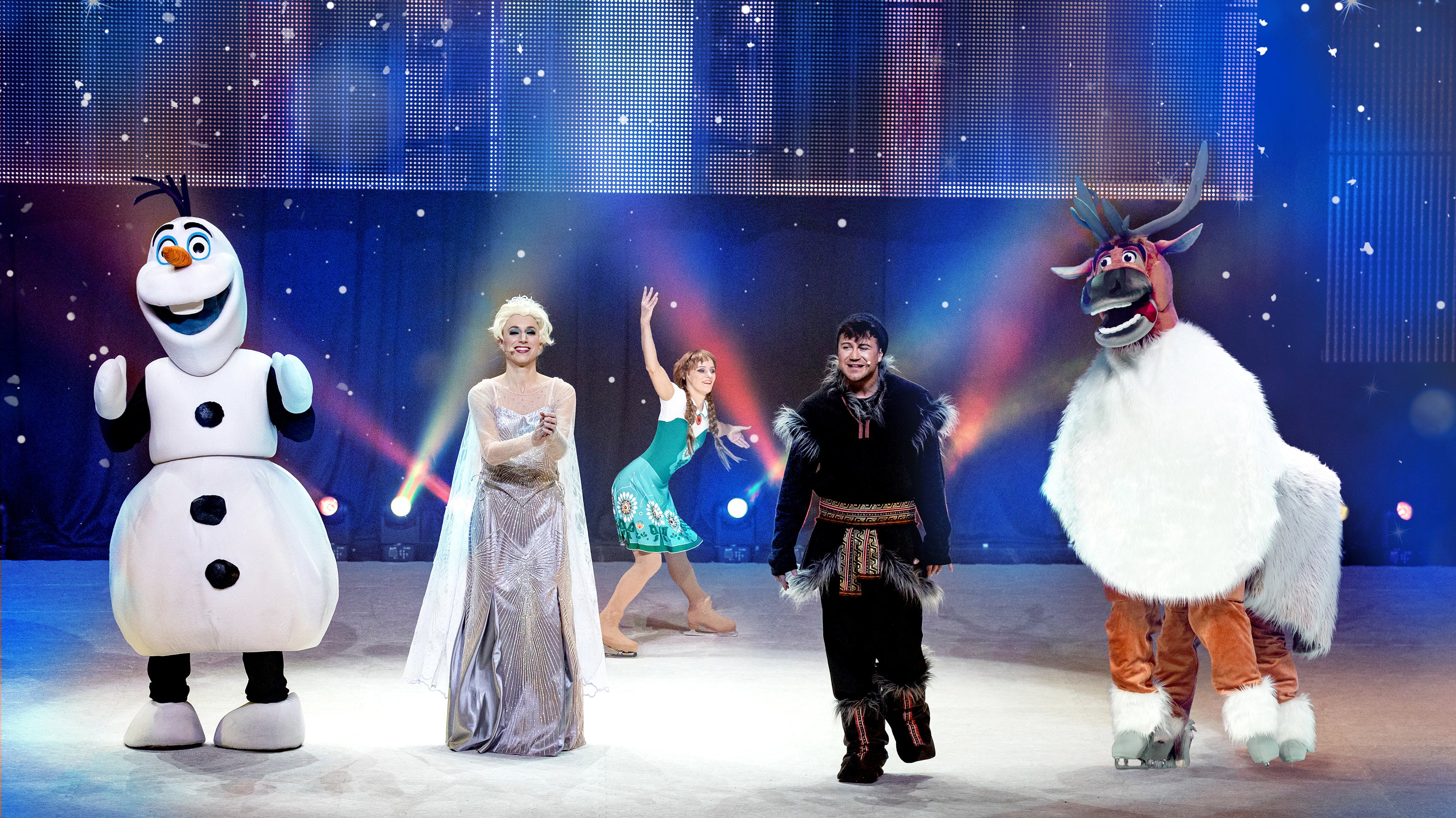 Blauer Hintergrund, im Vordergrund die Darsteller auf der Bühne, von links Olaf der Schneemann, daneben die Eiskönigin, daneben Christoph und ganz rechts das Rentier Sven
