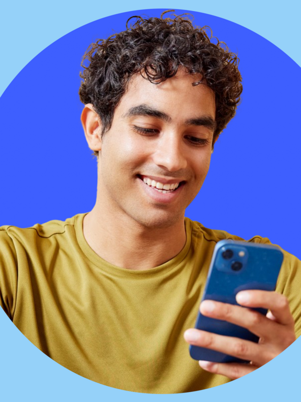 Mann mit braunen locken und einem lächeln hält ein Handy in der linken Hand und trägt ein gelbes Shirt