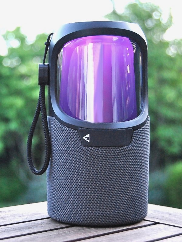 Eine kleine schwarze Musikbox steht auf dem Tisch. Im Hintergrund sind grüne Blätter. 