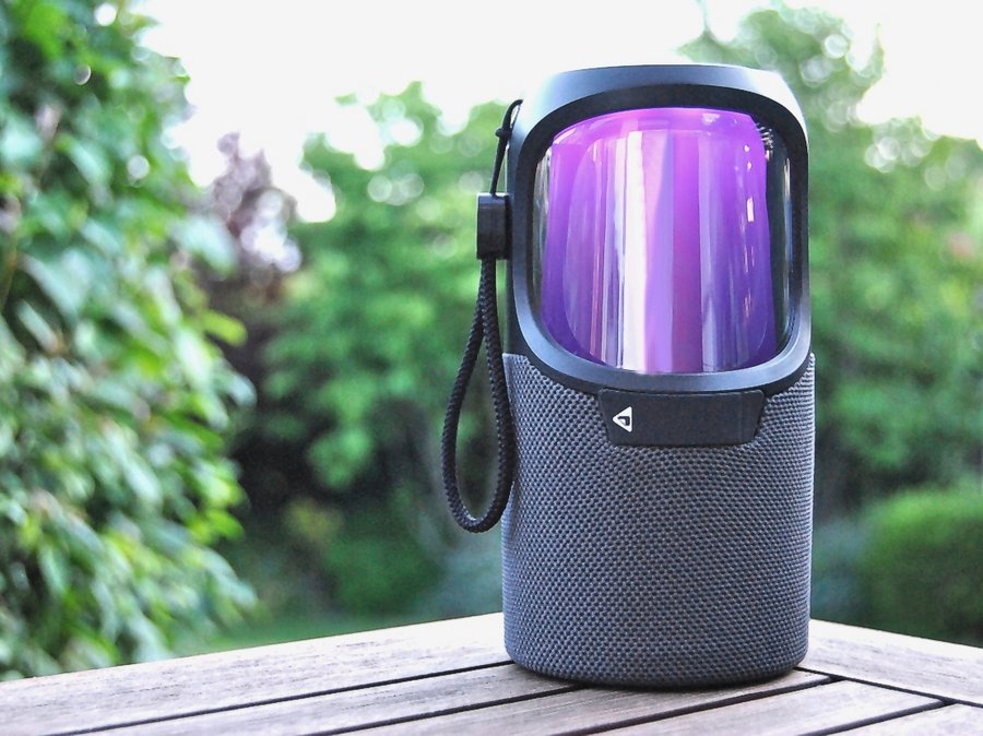 Eine kleine schwarze Musikbox steht auf dem Tisch. Im Hintergrund sind grüne Blätter. 