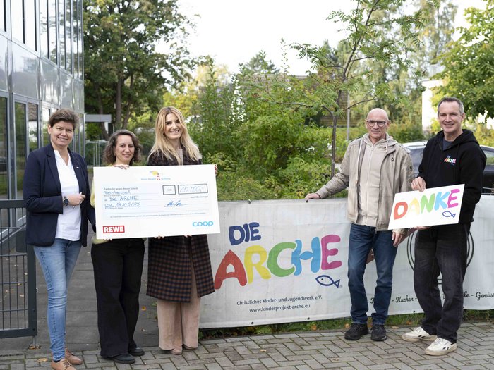 Mitarbeiterinnen und Mitarbeiter von der coop, REWE und Arche halten einen offiziellen Spendencheck im Wert von 10.000 Euro in die Kamera. 