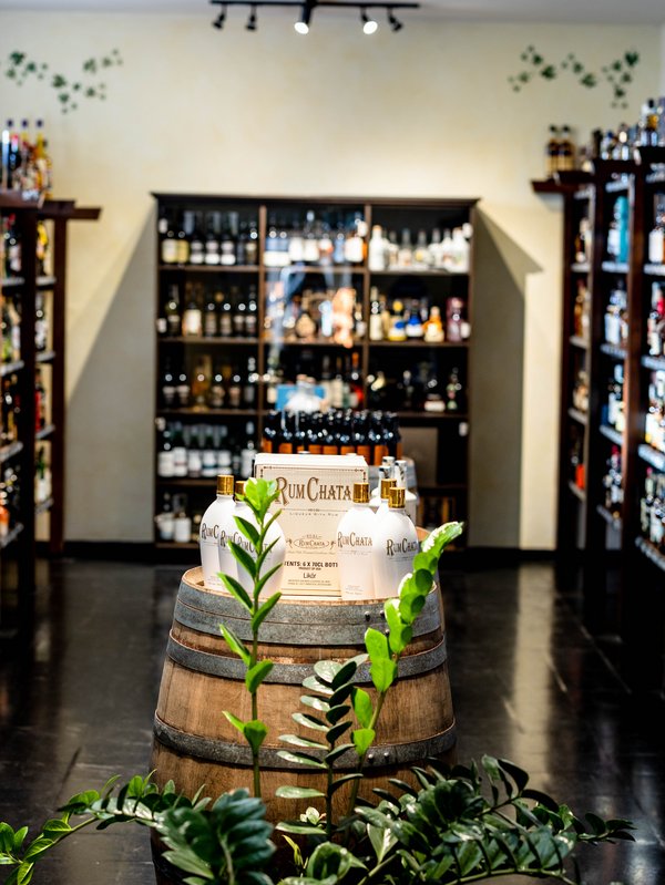 In der Mitte ist ein Eichenfass. Um das Fass herum sind dunkle Holzregale, die mit Weinflaschen gefüllt sind. 