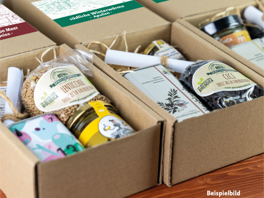 Kartons mit verschiedenen Adventsboxen. Die vorderen Boxen sind geöffnet und beinhalten Olivenöle, Gewürze und Spezialitäten