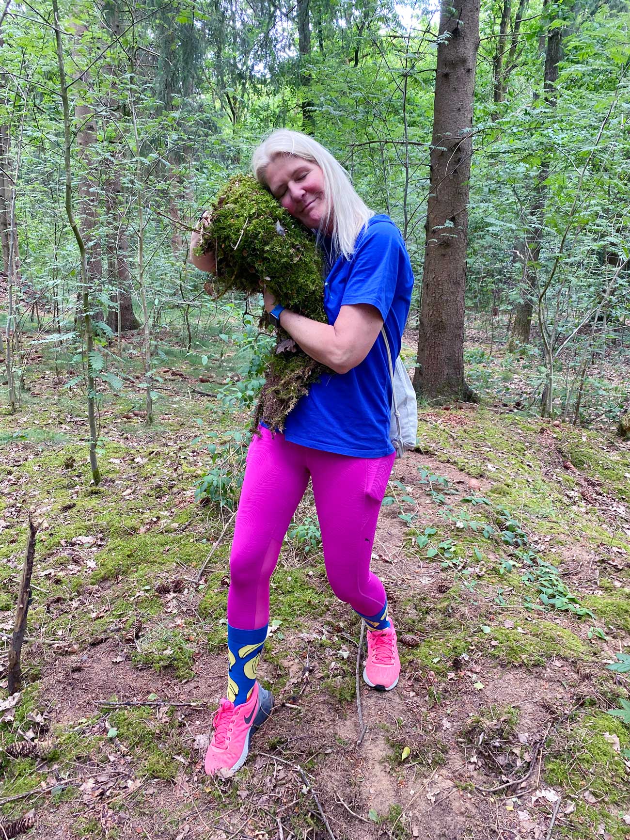 Corinna aus der Mitgliederbetreuung hält einen großen Moosteppich in den Händen und legt ihren Kopf darauf ab, um zu teste, wie weich dieser ist.