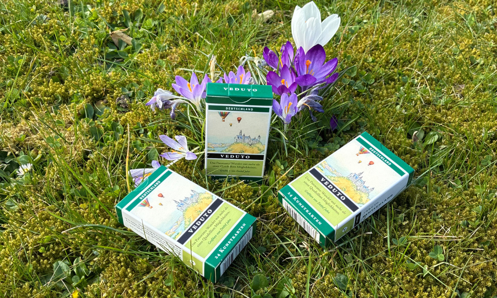 Auf dem Bild sieht mein drei von en exklusiven Kartendecks von dem künstler Detlef John. Sie liegen im Rasen. Im Hintergrund sind Blumen.