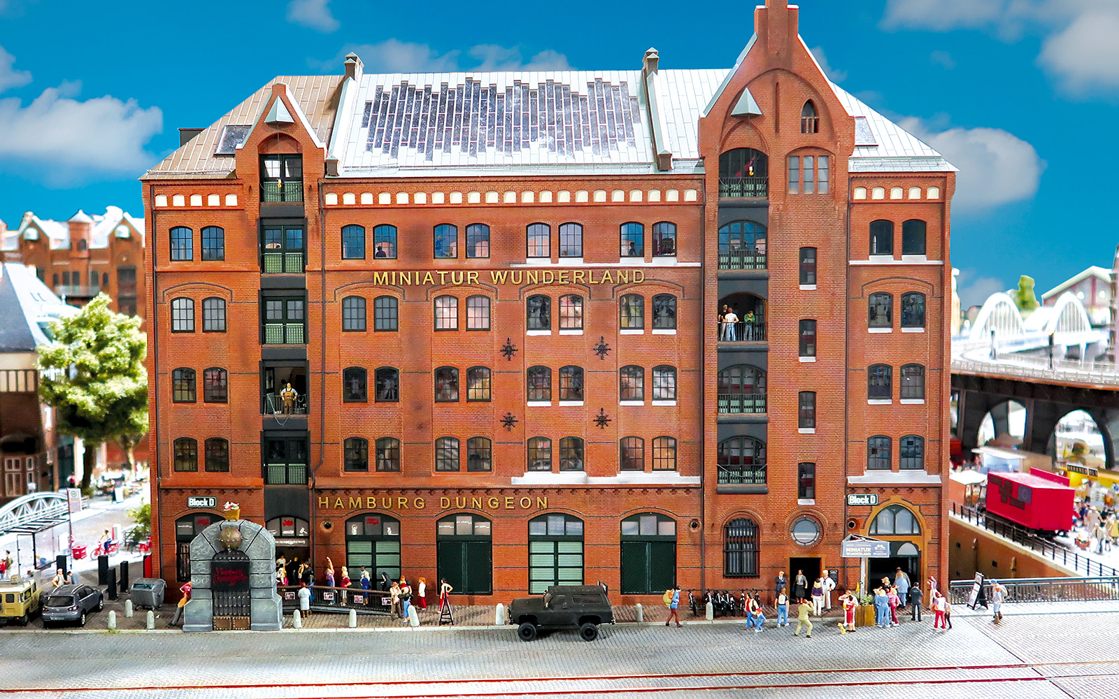 Nachbildung Miniatur Wunderland. Großes, rotes Backsteinhaus in der HH Speicherstadt mit goldenem Schriftzug Miniatur Wunderland, blauer Himmel, Schäfchenwolken